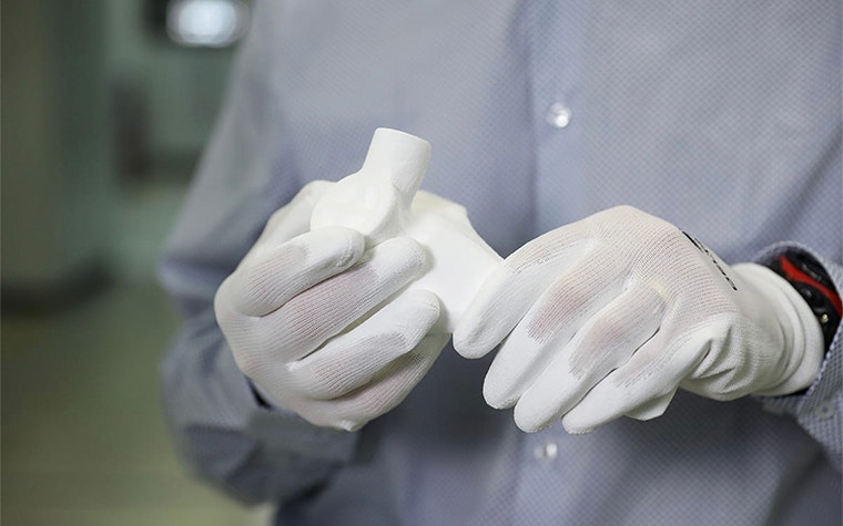 Person wearing gloves holding a 3D-printed component for oxygen masks