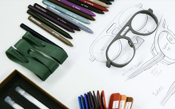 occhiali stampati in 3D e campioni con matite e penne colorate sopra un disegno di progetto