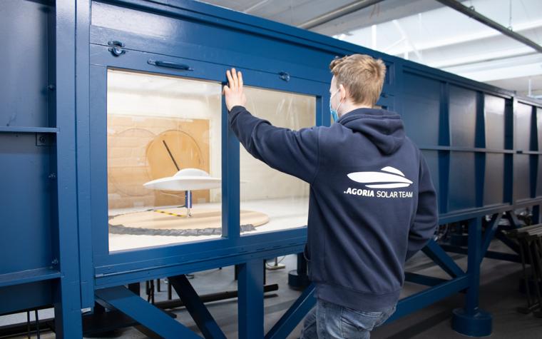 A student from the Agoria Solar Team observes a white 3D-printed model of the Solar Car in a wind tunnel.