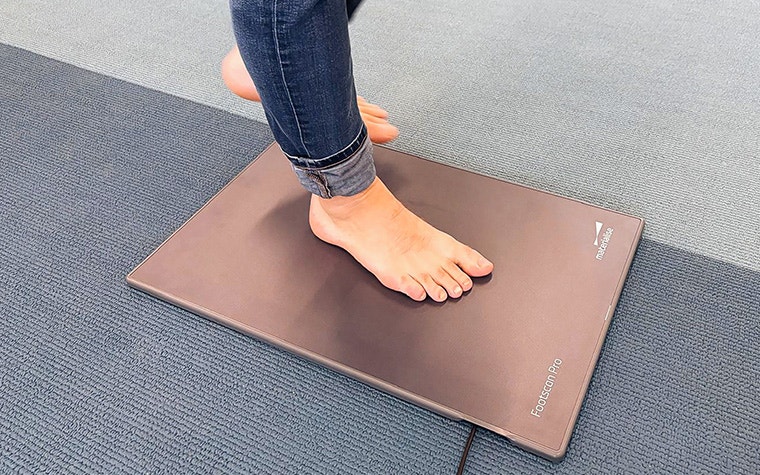 A barefoot man in blue jeans standing with one foot on the Materialise Footscan Pro Level pressure plate.