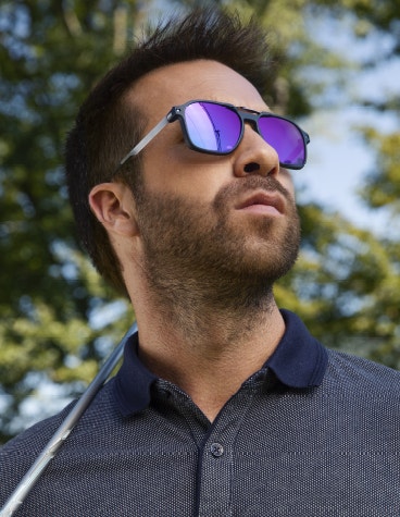 Homme avec un club de golf sur l'épaule, regardant vers le haut, portant des lunettes de soleil McLaren Vision Openmatic