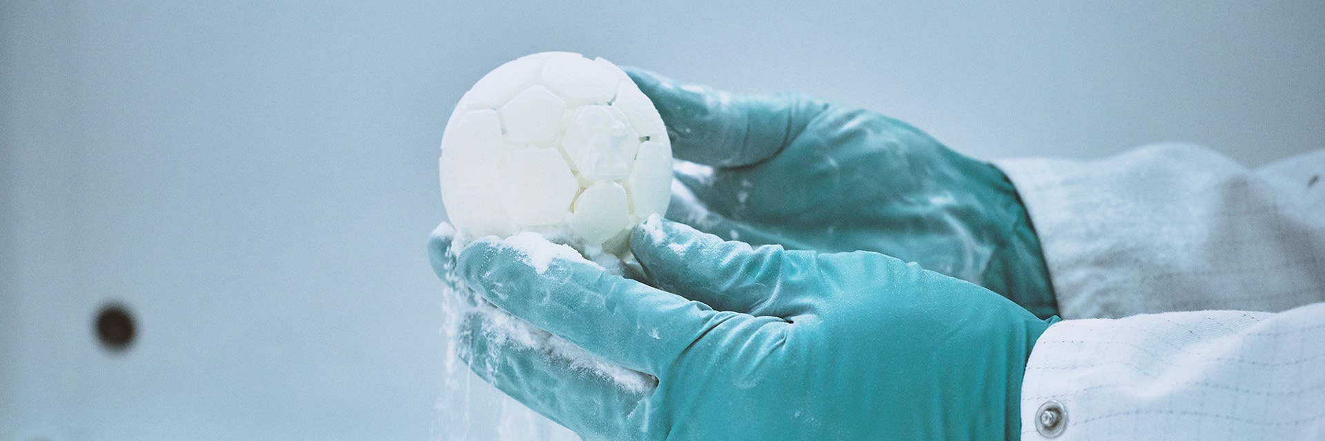 Gloved hands holding a 3D-printed ball with 3D printing powder falling from it