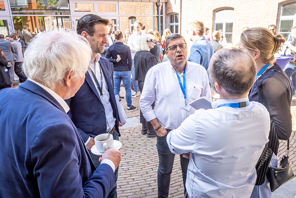 Five people standing in conversation in a courtyard at the Materialise 3D Planning and Printing Forum (2025), including Materialise Founder Fried Vancraen, holding a cup of coffee.