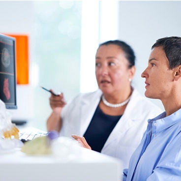 Un professionnel de santé pointant vers un écran d'ordinateur tout en parlant à un patient