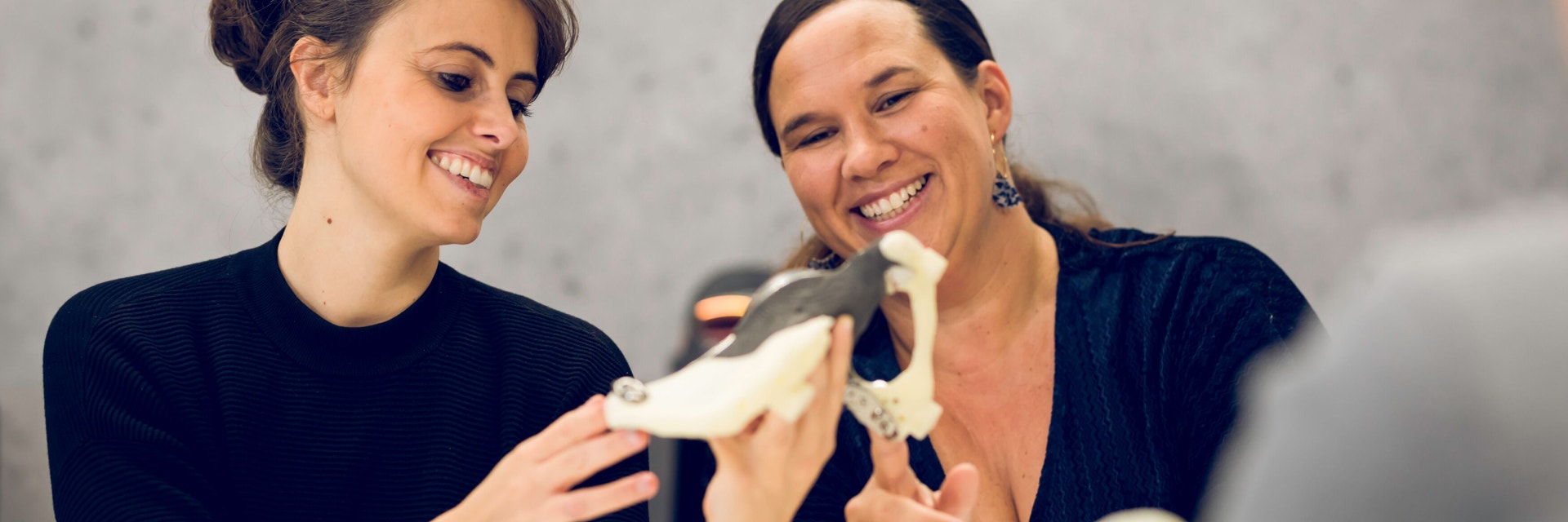 Dos mujeres sonrientes que miran a una pieza impresa en 3D
