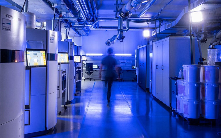 A person walking down a corridor in a dark 3D printing lab.
