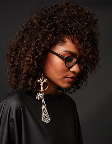 Black female model looking down, wearing statement earrings and black eyeglasses from Hoet Cabrio PZ