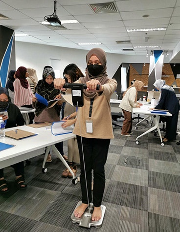 A female Materialise Malaysia employee standing on a machine during a wellness check