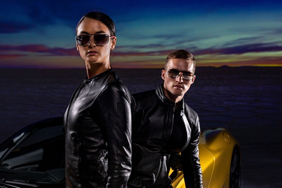 Two models in front of a McLaren sports car wearing 3D-printed sunglasses from the McClaren Vision Collection