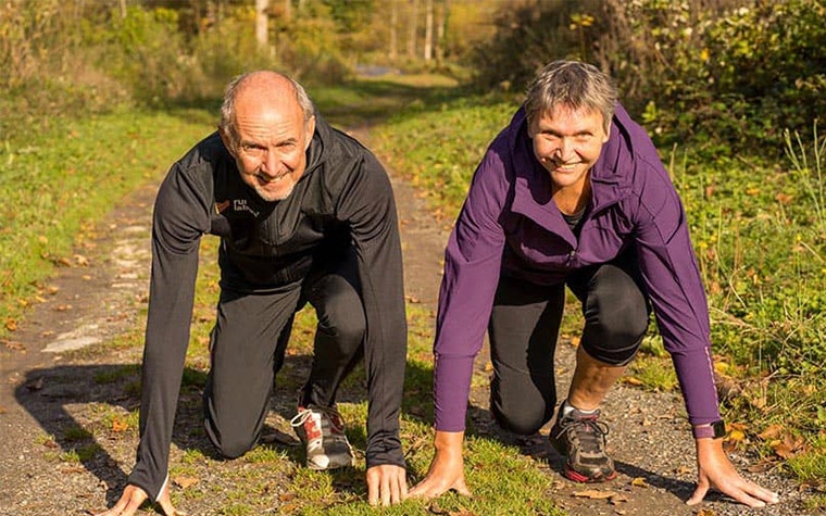 Two people smiling and kneeling on the ground, in a position where they're ready to run