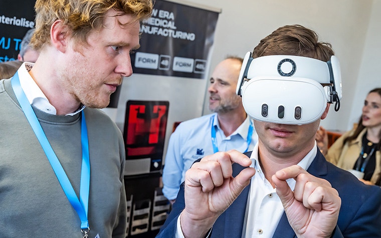 A man watching another man wearing an augmented reality headset. The wearer is holding both hands up in a pinching position.
