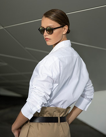 Modelo femenino posando y mirando por encima del hombro mientras lleva unas gafas de sol de la colección Hoet Cabrio PR