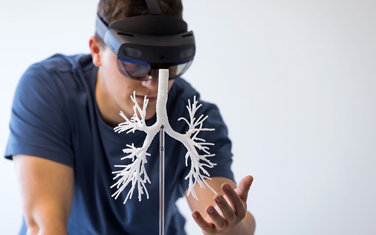 Mann trägt eine Augmented-Reality-Brille, während er ein 3D-gedrucktes Lungenmodell in die Hand nimmt