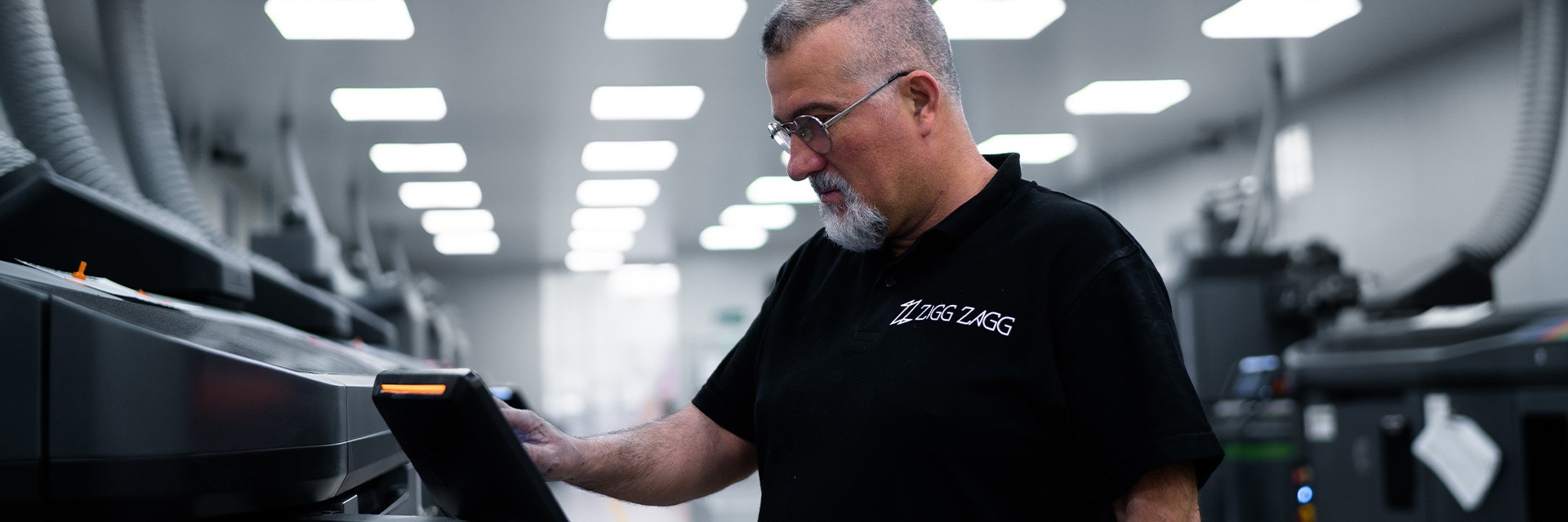 A man wearing a black Ziggzagg t-shirt pressing buttons on a screen that's connected to a 3D printer.