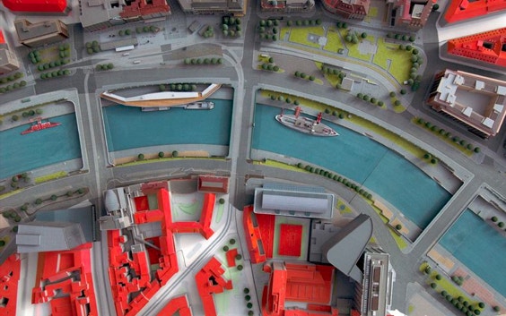Overhead view of a colorful city model including a canal, boats, roads, and buildings