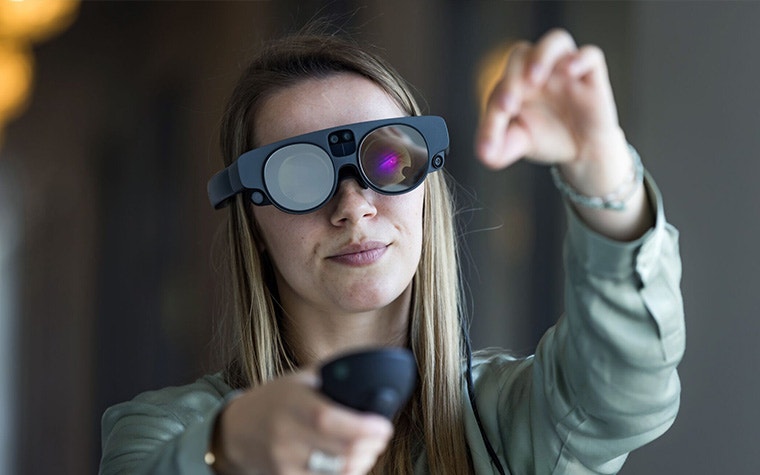 Woman wearing Magics Leap 2 AR goggles and holding a remote with the other hand extended in front of her