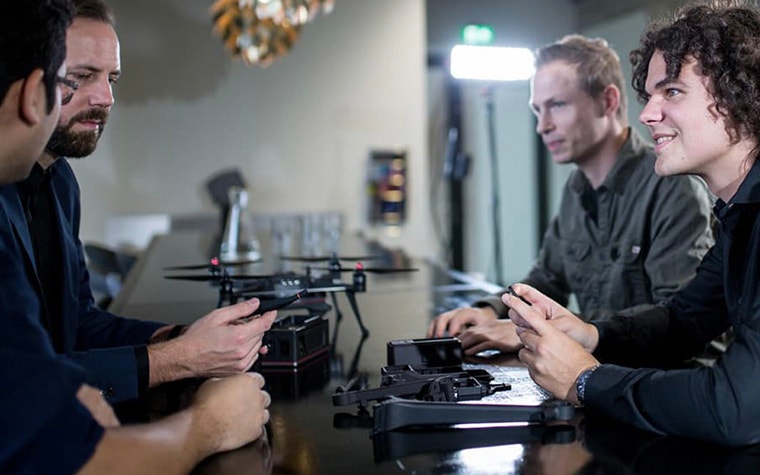 Four people sitting at a long table with drone models on the table between them 