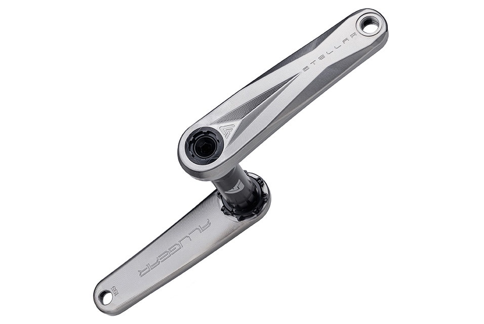 A polished titanium bicycle crankset without a chainring, featuring “STELLAR” engraved on the right arm and “ALUGEAR” on the left arm, displayed against a white background.