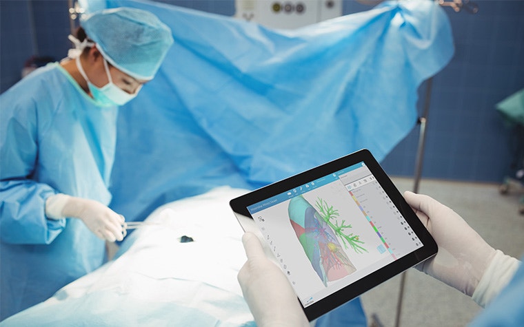 Surgeon holding a tablet in the OR and reviewing digital plan for thoracic surgery with Mimics Planner while another surgeon prepares the patient for surgery