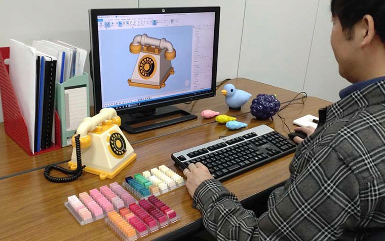 Man sitting at a desk, viewing a 3D model in magics next to a toy phone and color samples