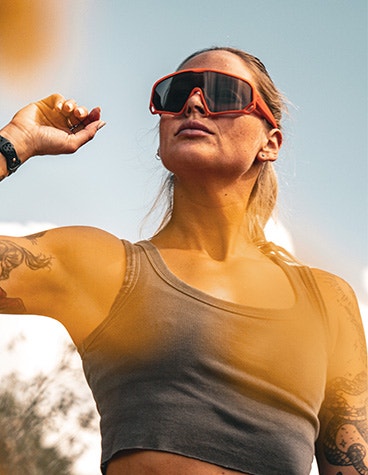 A woman outdoors wearing Zirkel's bright orange 3D-printed Teddy Grizz eyewear with a black visor.