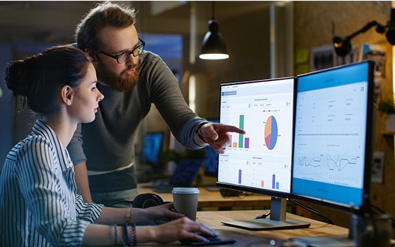 Two people at a desk looking at computer monitors with CO-AM software