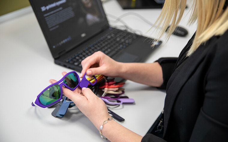 A Materialise Project Engineer hold a pair of sport sunglasses and compares swatches of colored plastic 