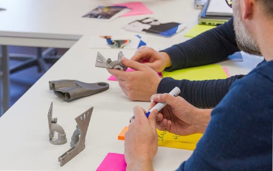 Büroangestellte, die 3D-gedruckte Metallteile auf einem Schreibtisch analysieren (Weitwinkel)