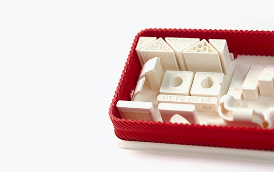 A series of white 3D-printed parts made from ABS-M30 using fused deposition modeling in a red box.