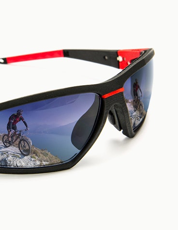 Schwarze und rote Sportbrille von SEIKO Xchanger, in der sich ein Mountainbiker spiegelt.