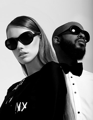Graustufenbild eines weißen weiblichen Modells und eines schwarzen männlichen Modells, die mit einer Hoet-Cabrio-Sonnenbrille posieren