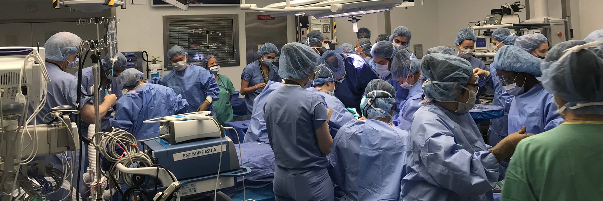 An operating room crowded with surgeons and clinicians wearing scrubs 