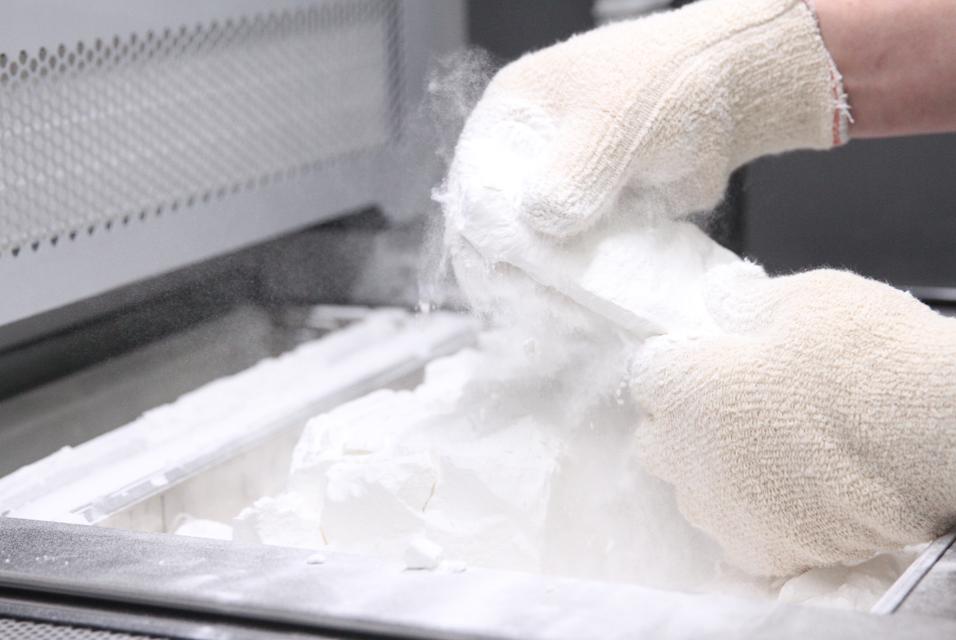 Gloved hands removing a 3D-printed part from powder