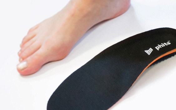 Nahaufnahme eines nackten Fußes neben einer 3D-gedruckten orthopädischen Phits-Einlage