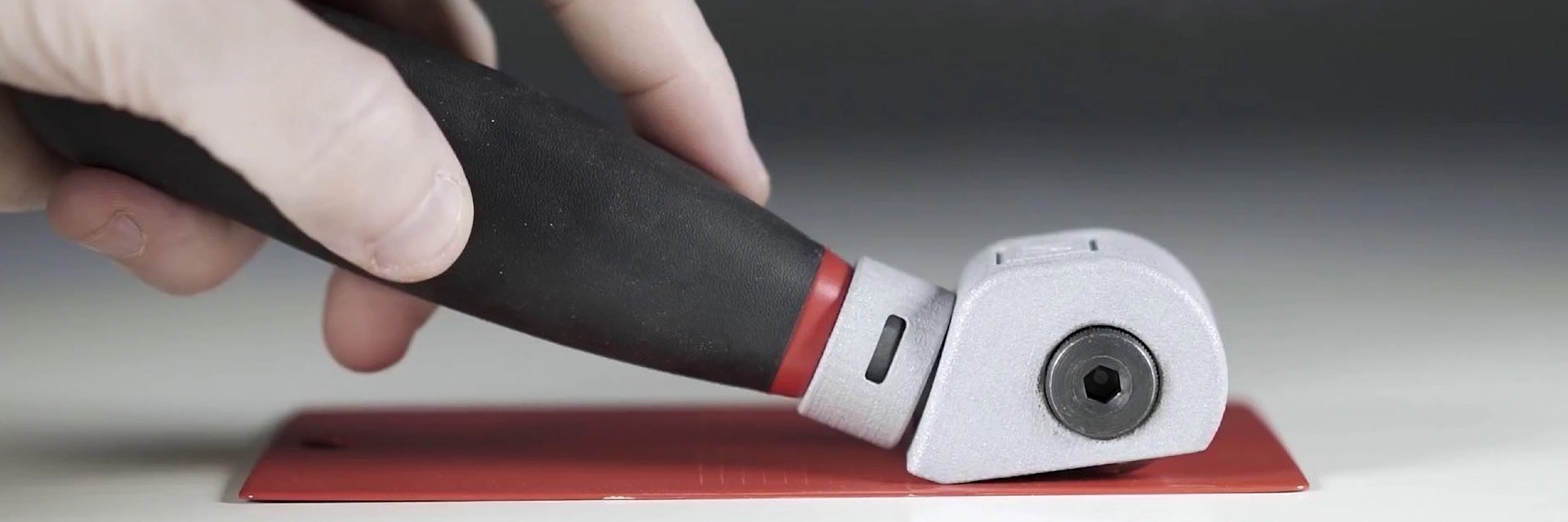 Eine Hand, die das NEURTEK-Schneidewerkzeug über eine rote Metallplatte zieht.
