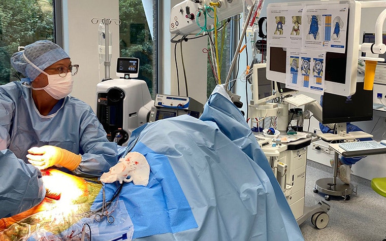 Two orthopaedic surgeons performing surgery on the patient while reviewing the surgical posters