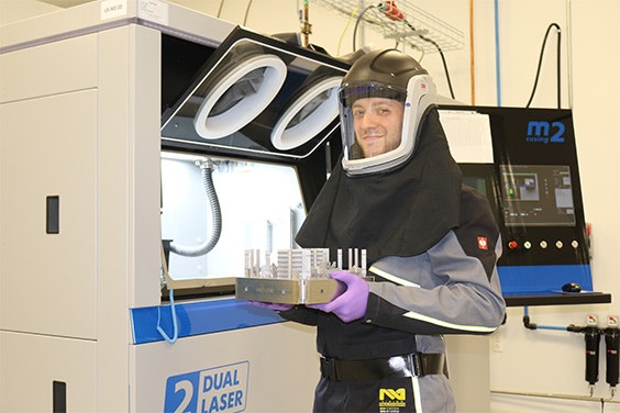 Materialise production worker holding a platform of metal 3D-printed parts recently removed from a 3D printer