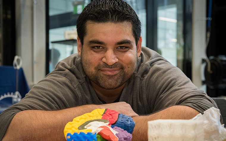 Dr. Mazher Iqbal Mohammed sits at a table with various colorful 3D-printed items in front of him 
