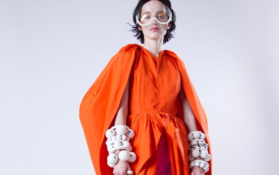 Model wearing an orange dress as well as artistic 3D-printed eyewear and bracelets