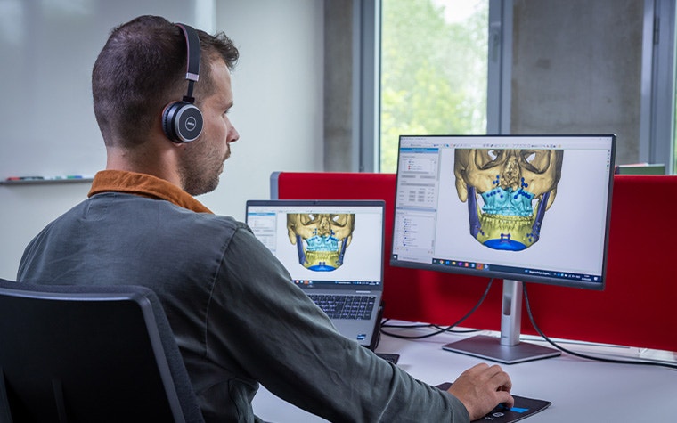 Ein Mann mit Kopfhörern schaut auf einen Computerbildschirm, auf dem die Materialise Enlight CMF-Software zu sehen ist.