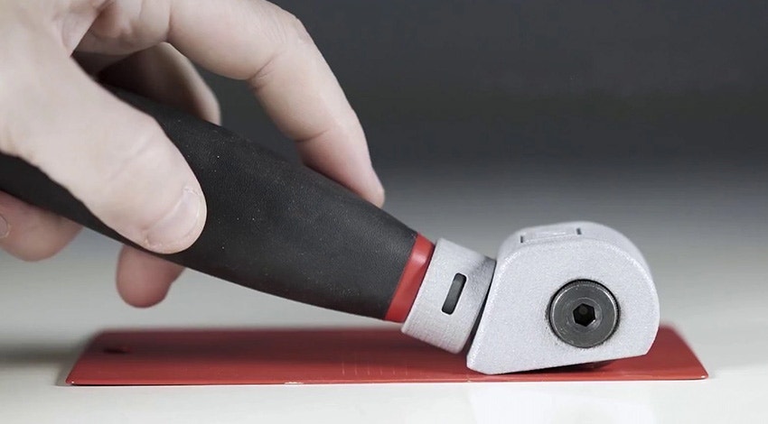 A hand dragging NEURTEK's cutting tool across a red sheet of metal.