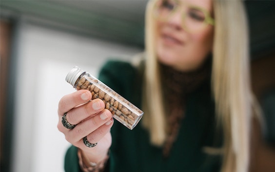  A woman wearing 3D-printed eyewear holds up a clear container filled with castor beans