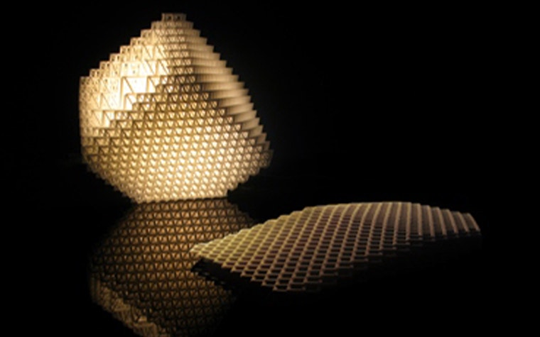 A cube-like, 3D-printed lamp lit up, made up of lattice structures