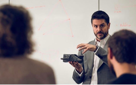 Kursleiter erklärend vor einer Klasse, während er ein 3D-gedrucktes Teil hält