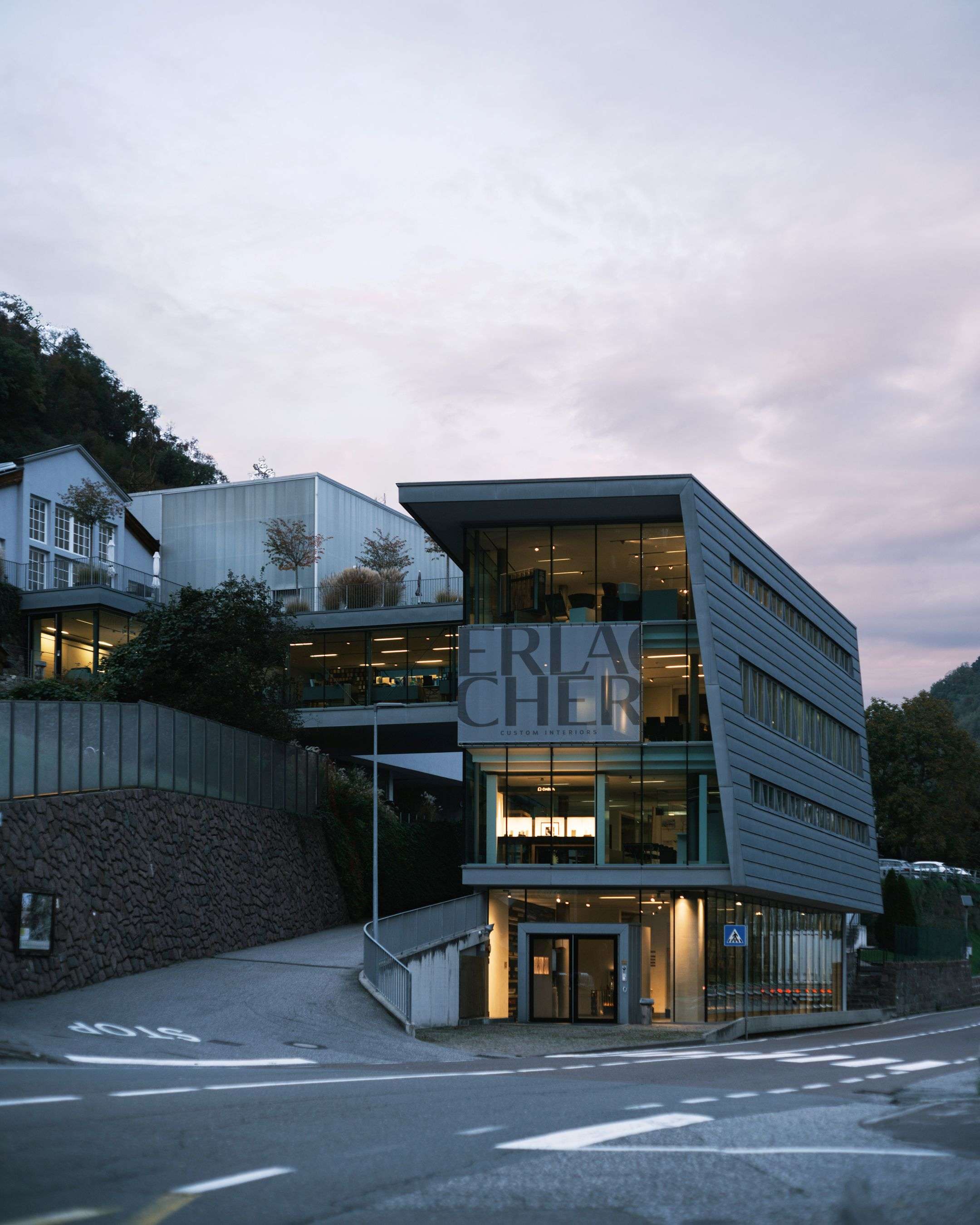 Modern company headquarters of Erlarcher with glass façades and metal cladding, illuminated interiors and clean architectural lines at dusk.