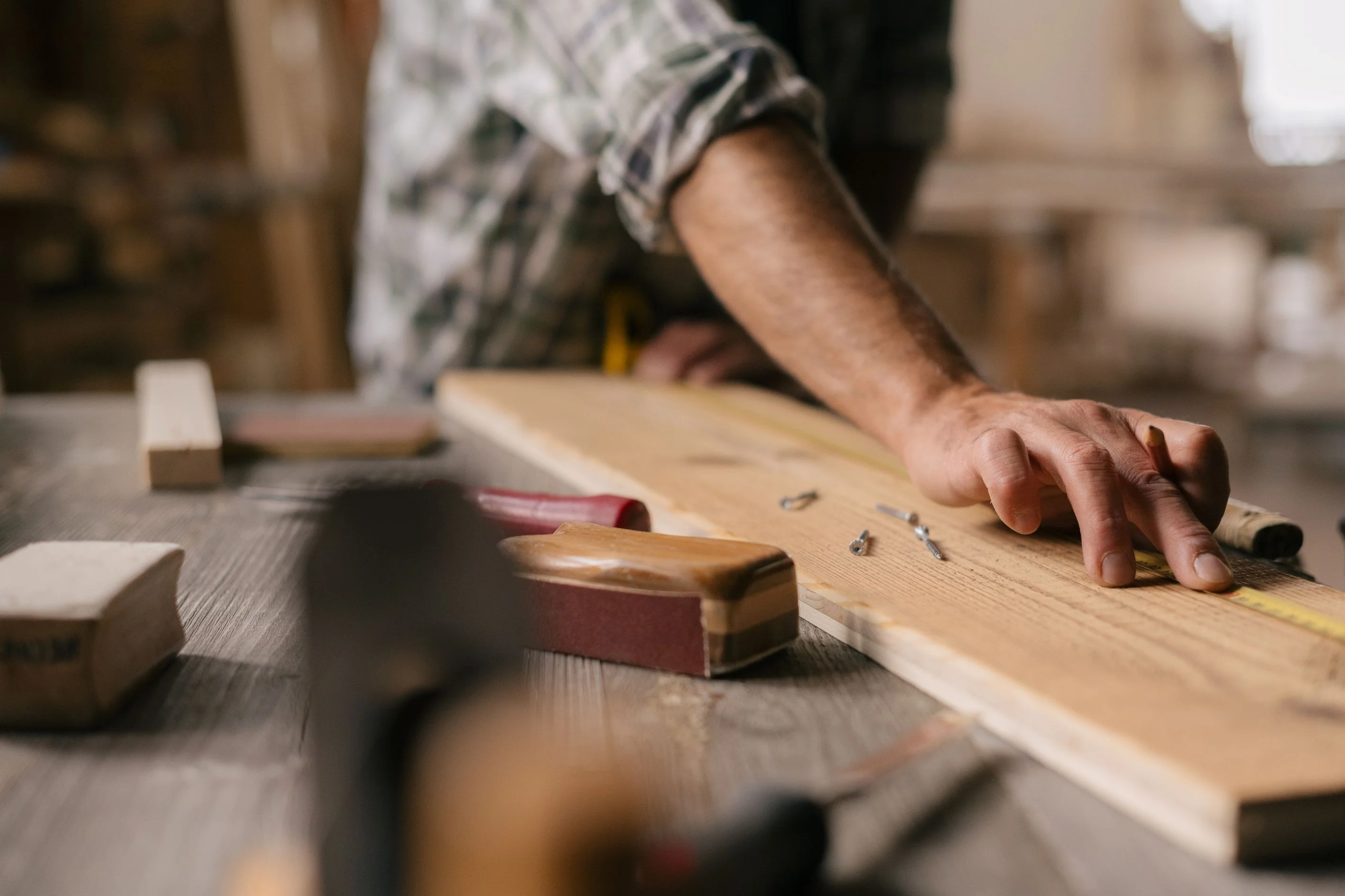 A hand resting on a wooden piece holding a measuring tape