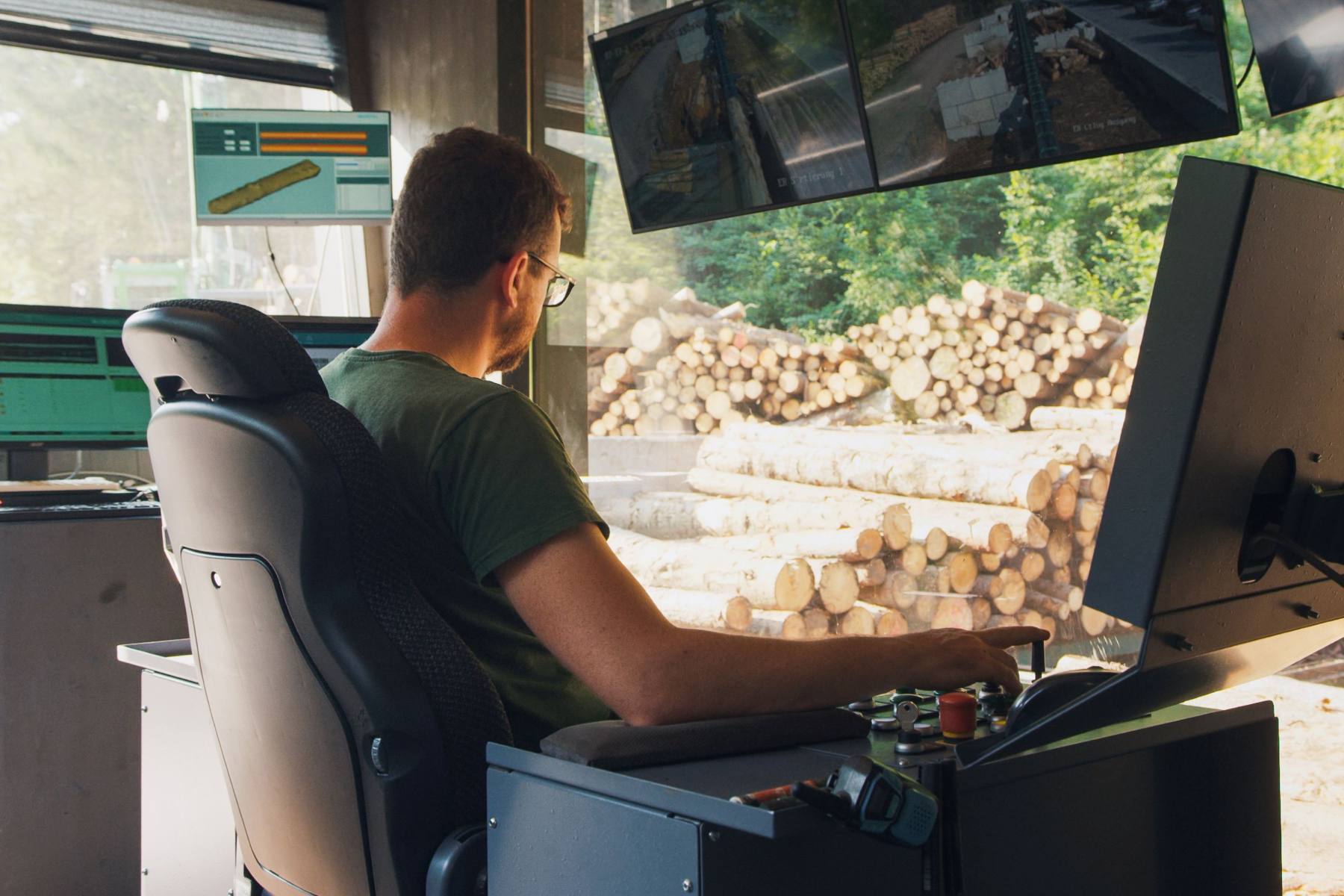 Man sitting in the control room looking at stacked logs