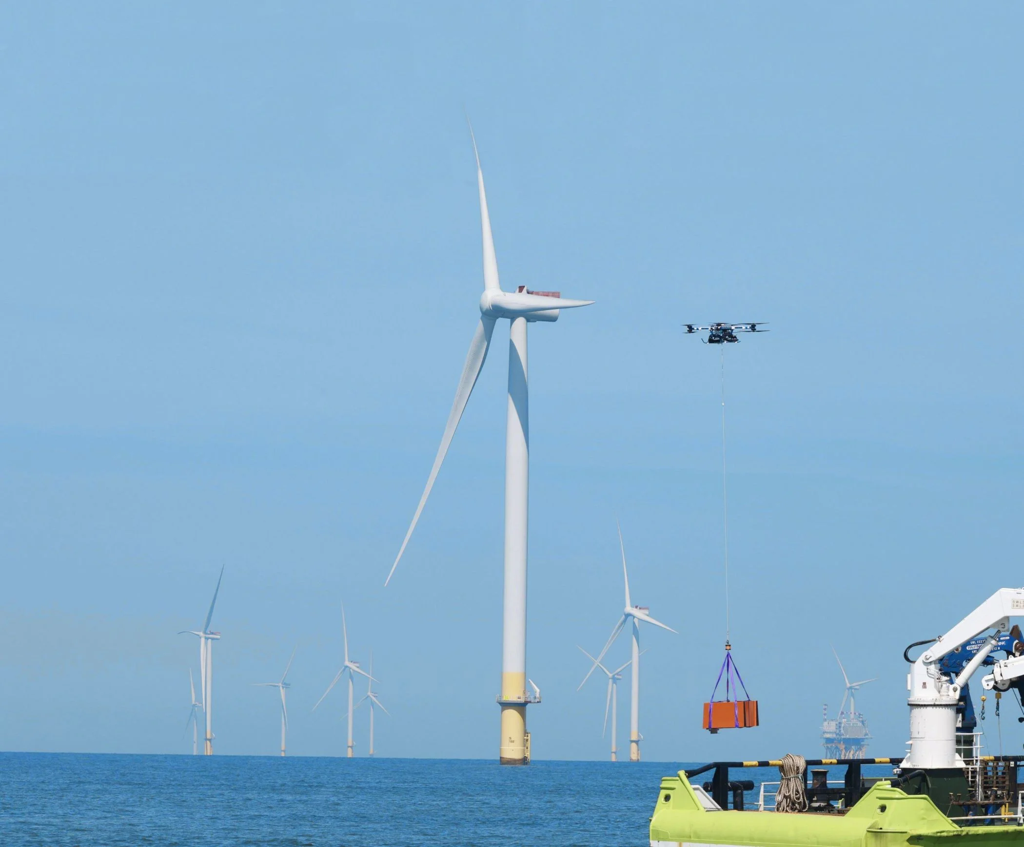 Offshore wind farm with cargo drone approaching while carrying a container