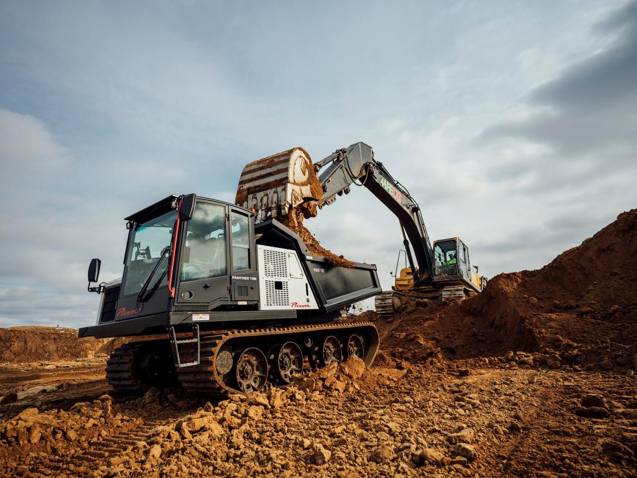 An excavator loading sand onto a large tracked vehicle