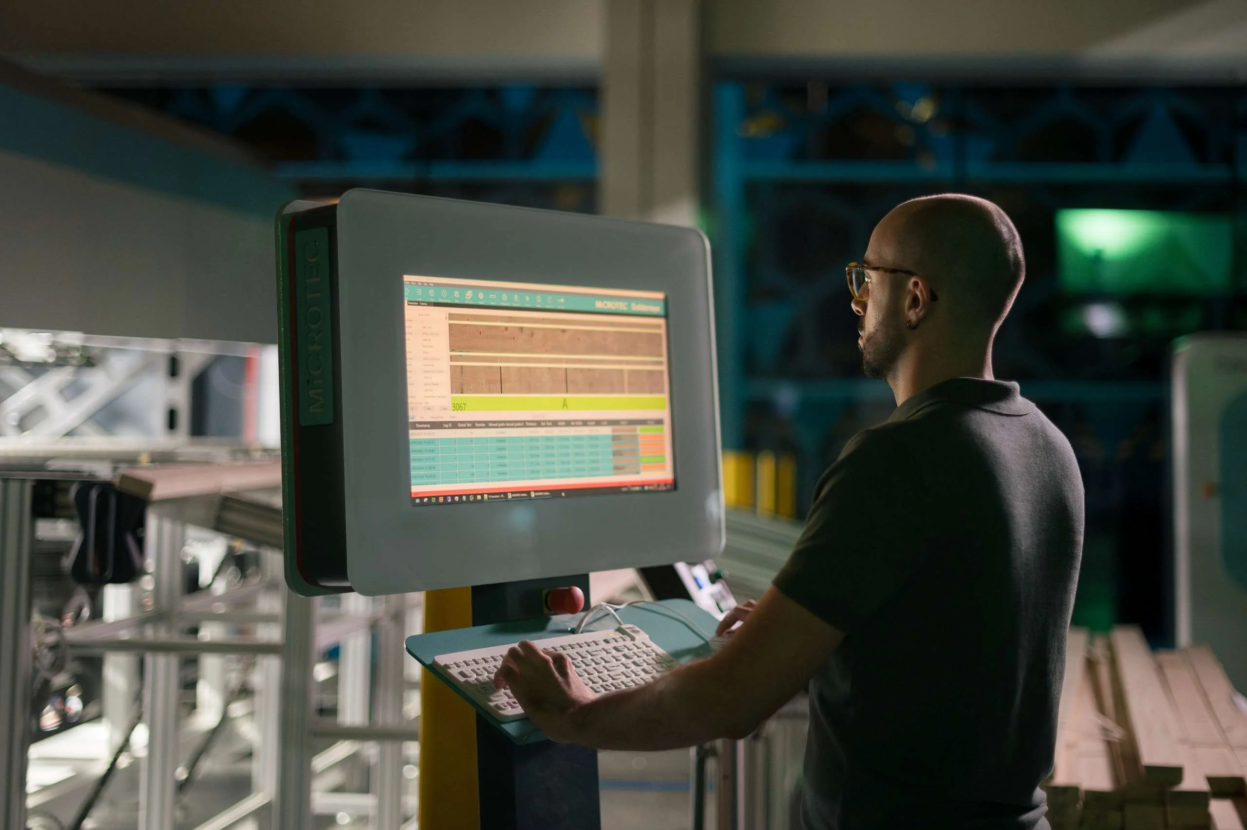 Man in a production hall standing in front of a screen and typing on the keyboard